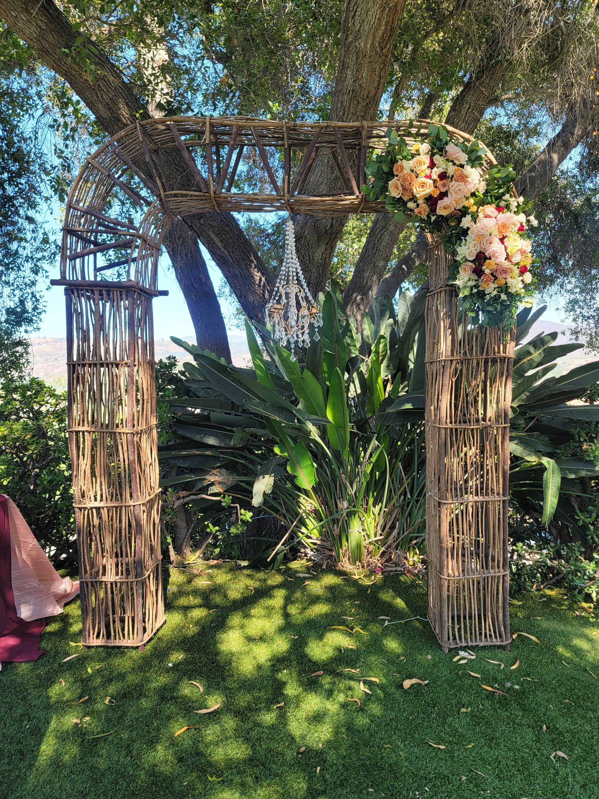 Wedding arch with floral decorations on a grassy lawn, under a tree.