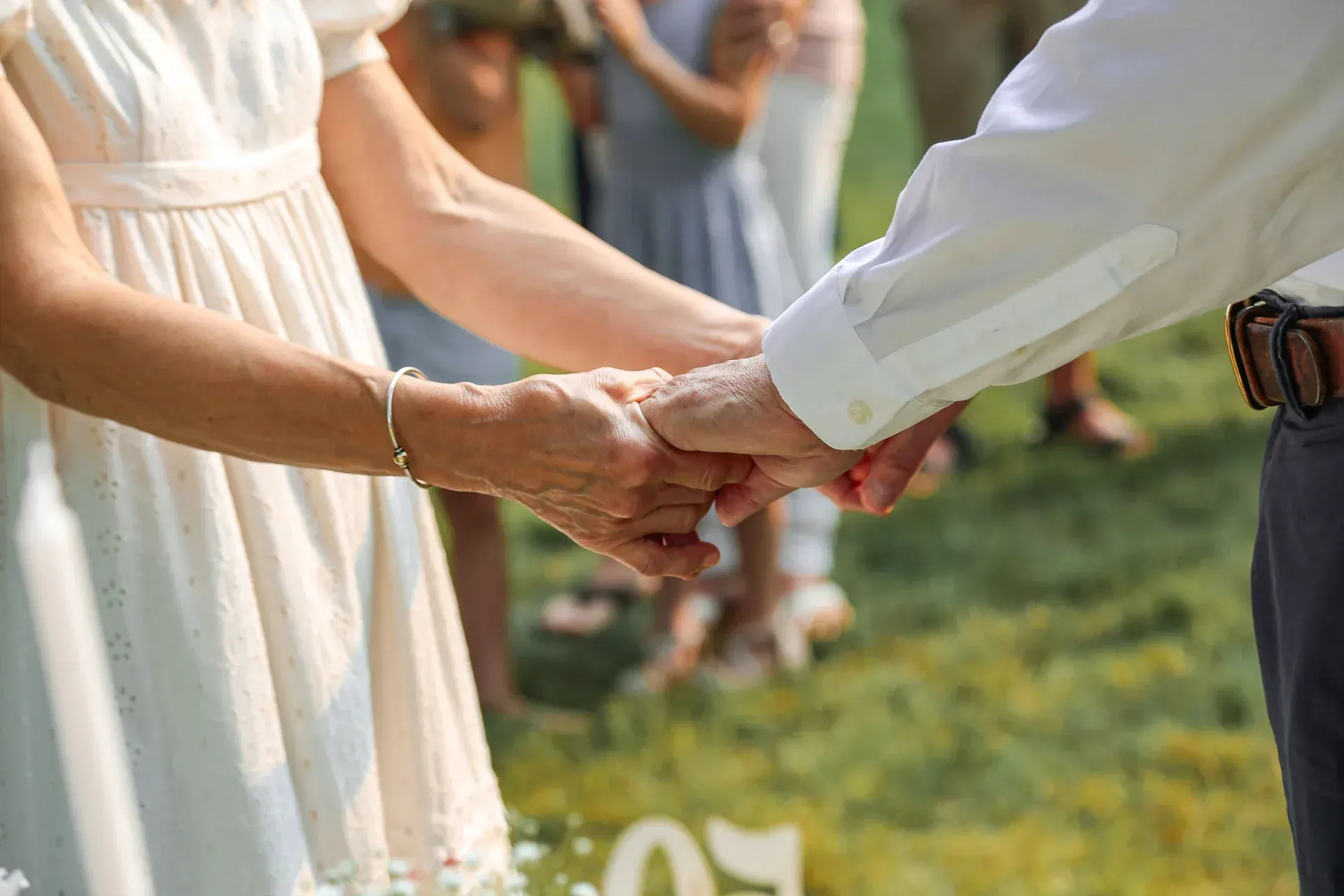Couple holding hands during a wedding ceremony outdoors, with a white dress and shirt.