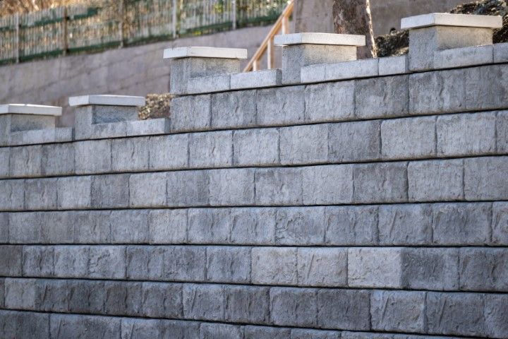 Block wall with evenly stacked rectangular blocks and capstones on top.
