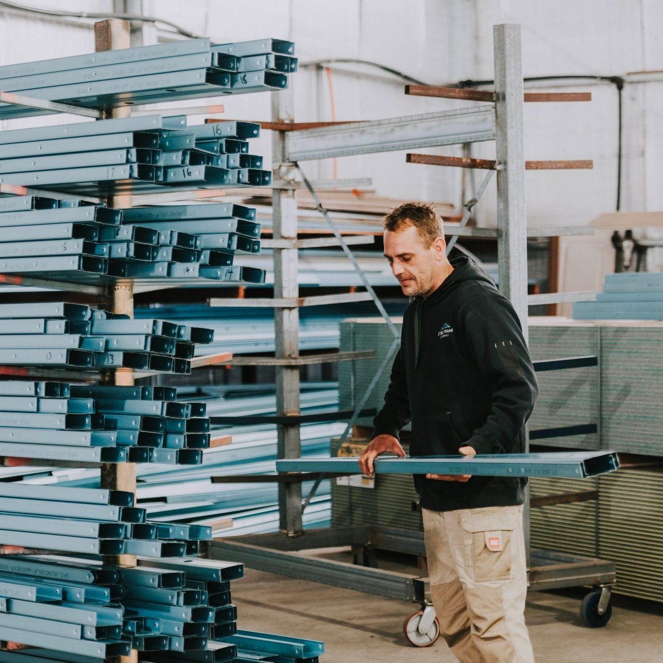 A Man is Standing in Front of a Stack of Blue Pipes — Steel Frame Company In Maitland, NSW