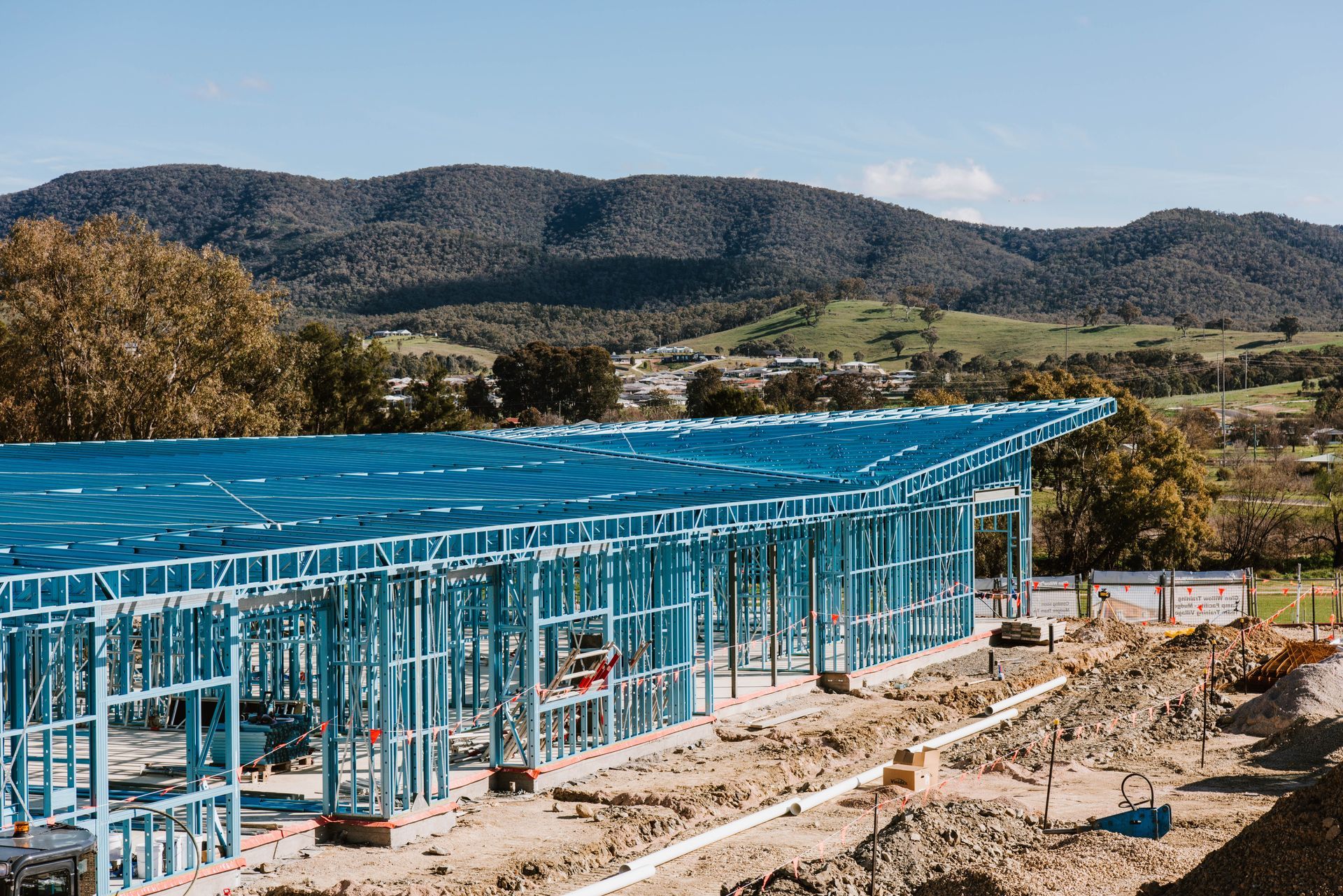 Blue-roofed steel building under construction with mountains in the background
