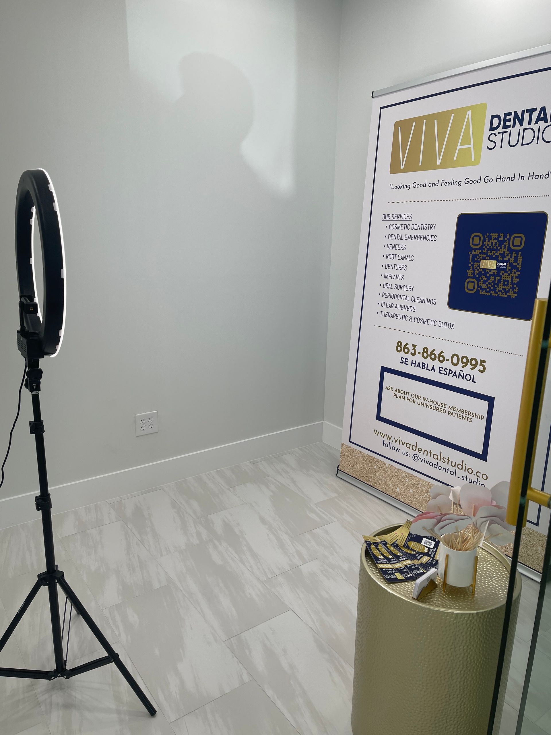 Ring light on a tripod, backdrop, and a small gold side table with a small sign in an empty room.