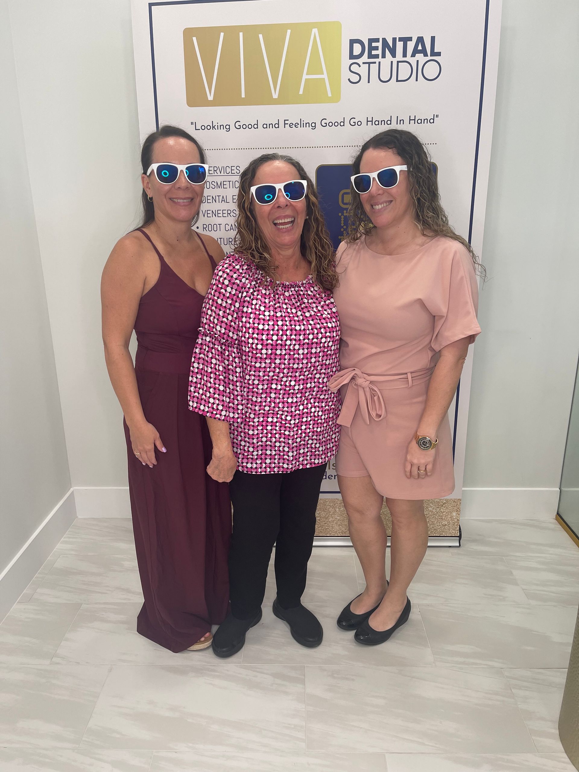 Three women wearing sunglasses pose in front of a 
