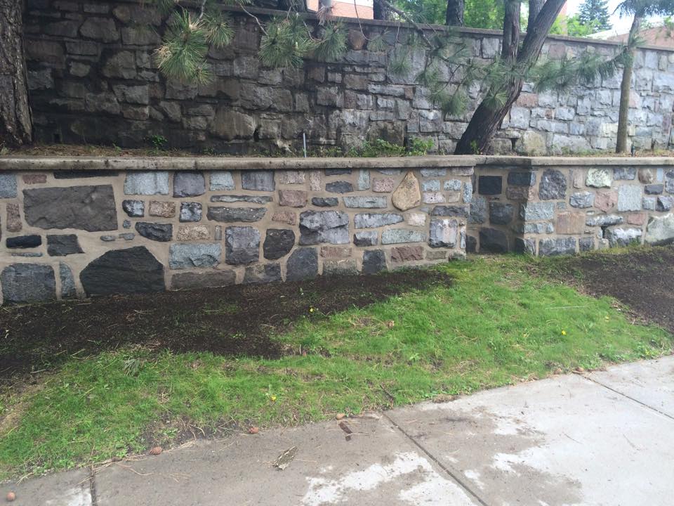 Un mur de pierre entoure une zone herbeuse à côté d'un trottoir