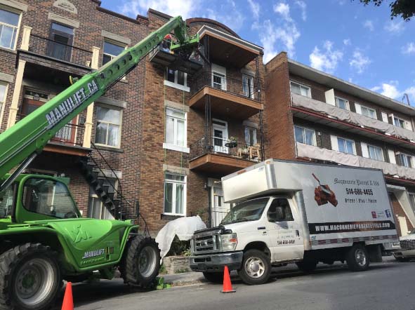 Un chariot élévateur vert et un camion blanc sont garés devant un bâtiment.