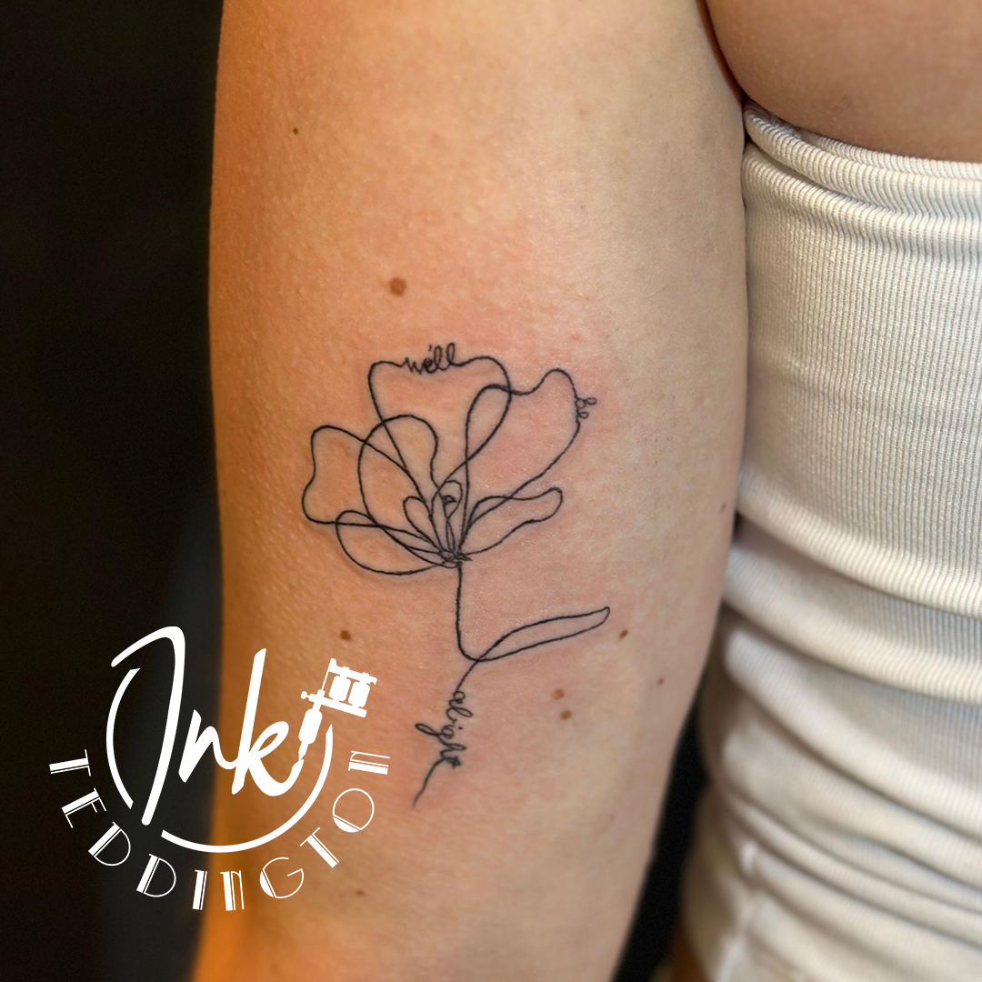 Line-art flower tattoo on a person’s upper arm, with a small watermark in the corner