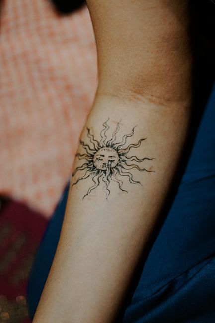 Close-up of a forearm with a small black sun tattoo near the wrist.