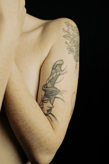 Close-up of an arm and shoulder with black line-art tattoos on a dark background
