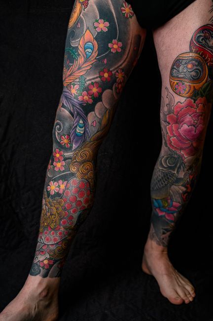 Colorful floral tattoos cover both legs against a black background, with one foot bare and visible.