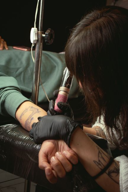 Tattoo artist in black gloves using a tattoo machine on a client's arm in a studio