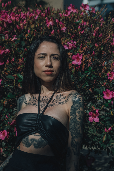 Woman in a black top standing before vibrant pink flowers, looking at the camera.
