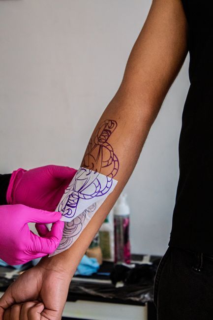 Artist outlining a forearm tattoo in purple ink while the arm rests on a table