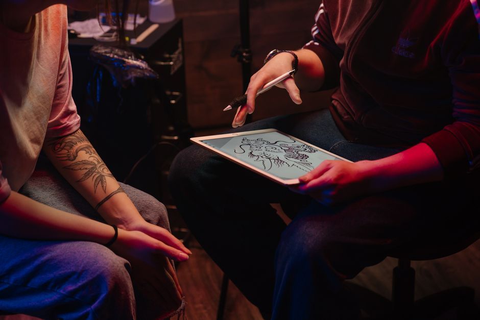 Two people seated in a dim room, one holding a tablet and stylus, discussing a design sketch.