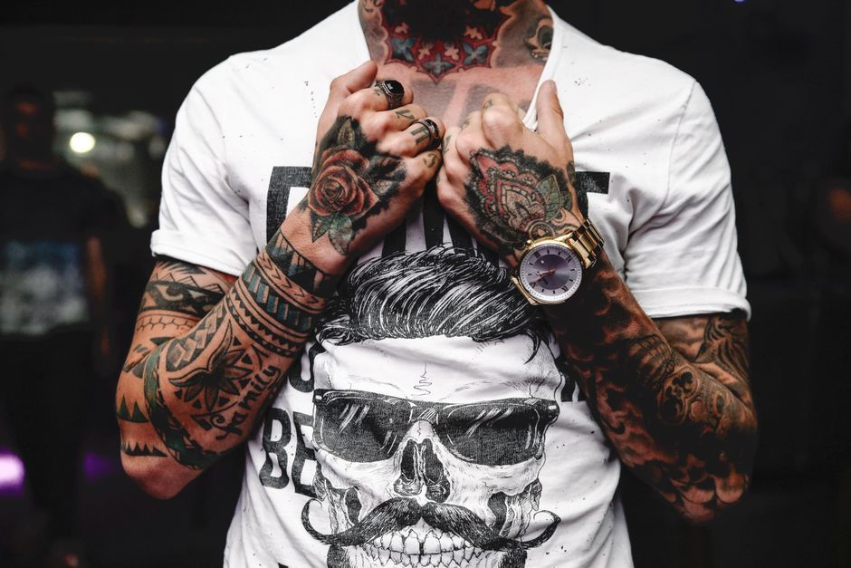 Tattooed person in a white skull T-shirt with hands clasped near their chest
