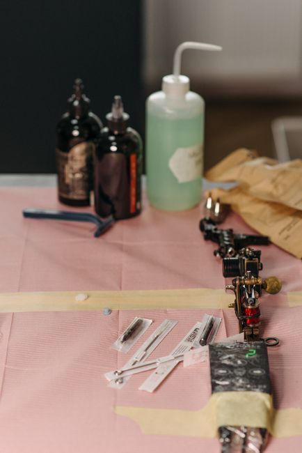 Tattoo setup with ink bottles, green wash bottle, and tattoo machine on a pink-covered work surface