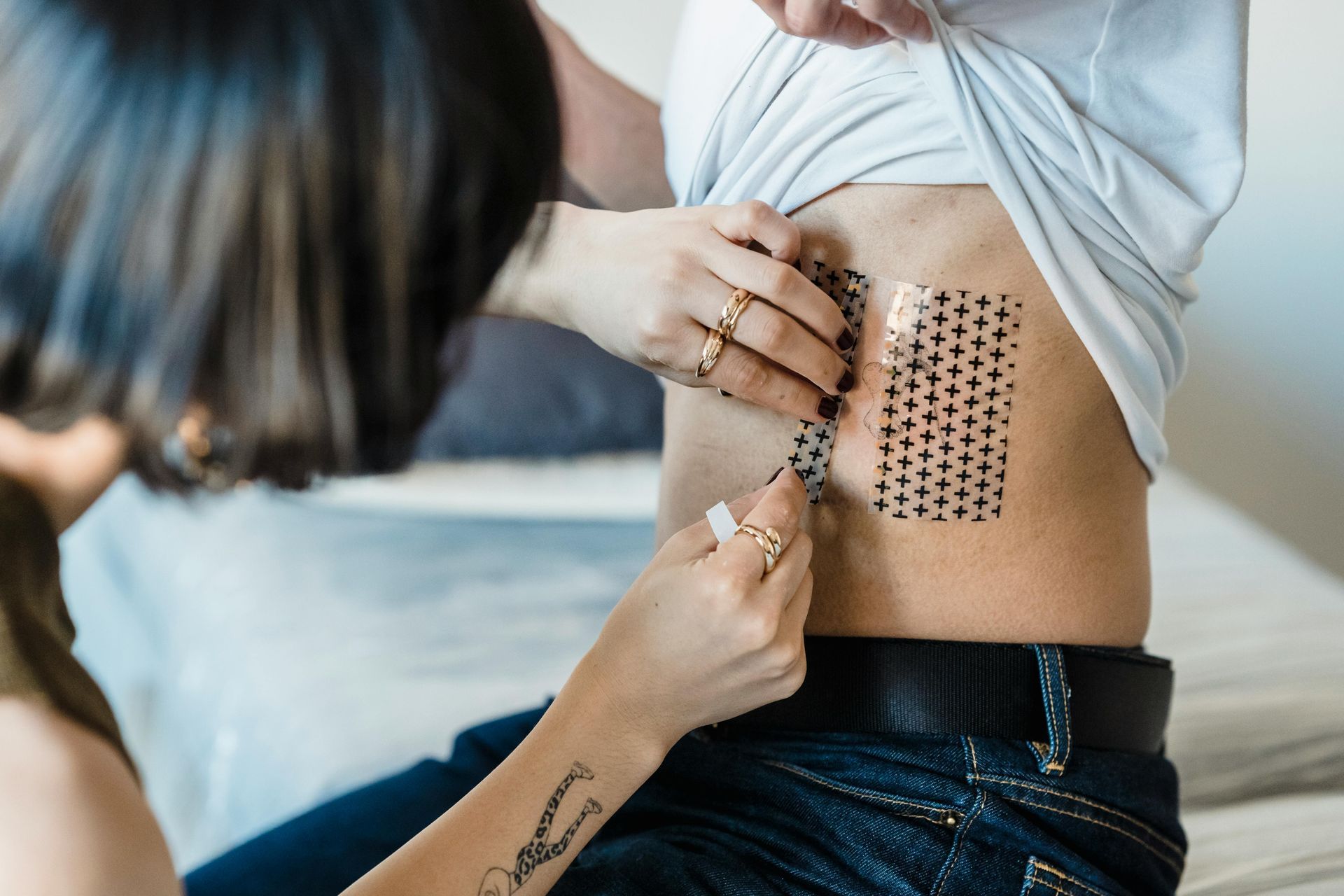 A person applying tiny black square stickers in a grid on another person’s side near the waist.