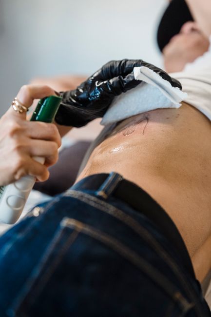 Person getting a tattoo on their hip with a black-gloved artist using a green machine.