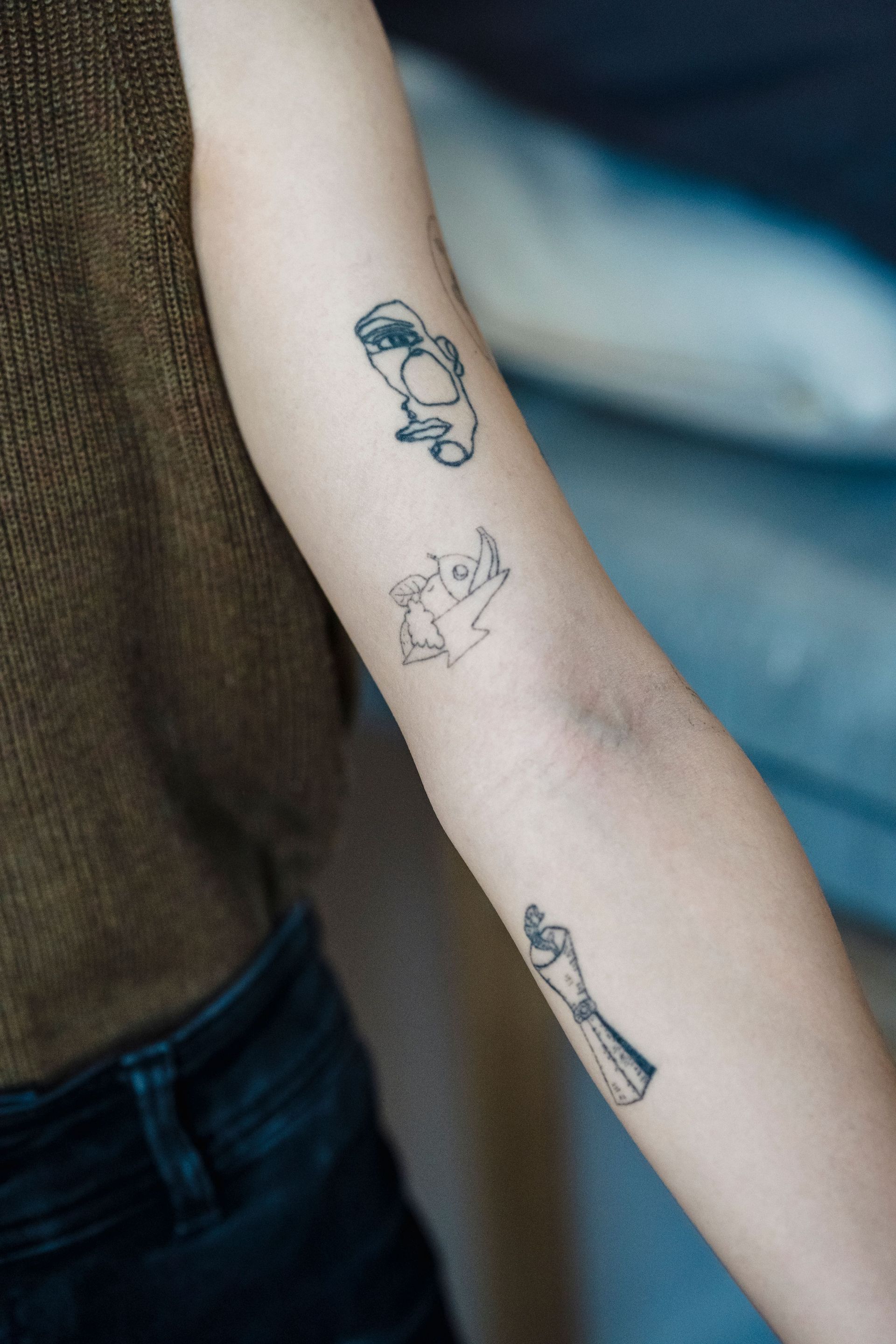 Forearm with three small minimalist tattoos on a brown sweater background