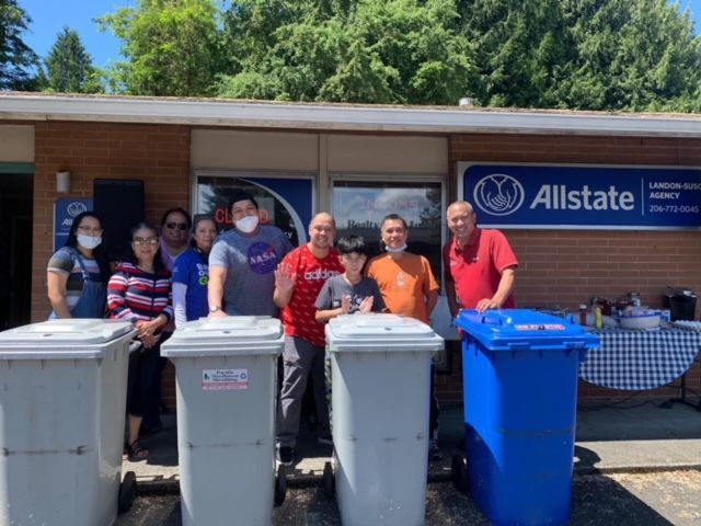 A group of people standing next to trash cans in front of an allstate building.