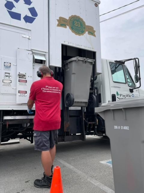 A man in a red shirt is standing in front of a recycling truck