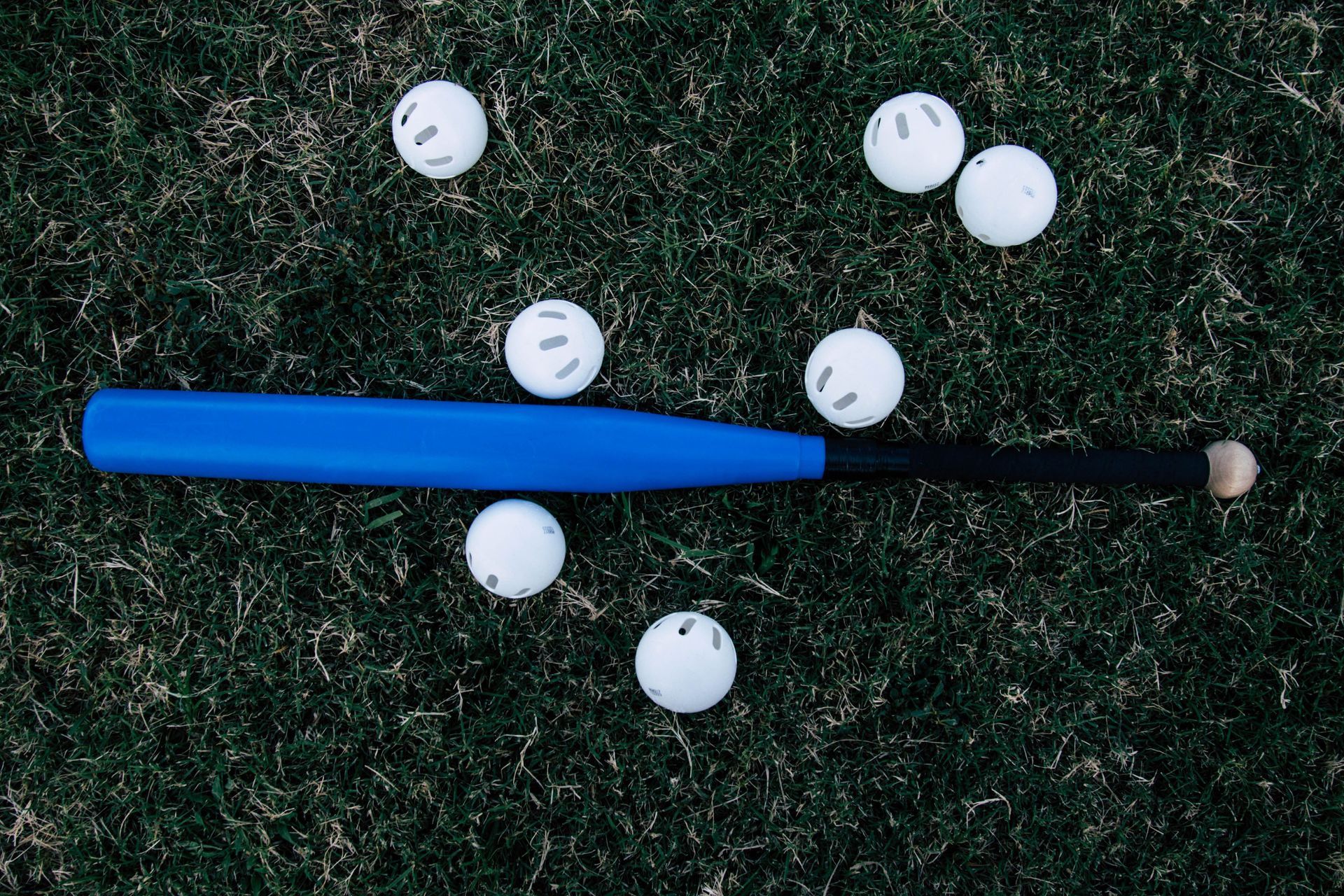 Baseball glove with ball on green grass, with blurred baseballs in the background.