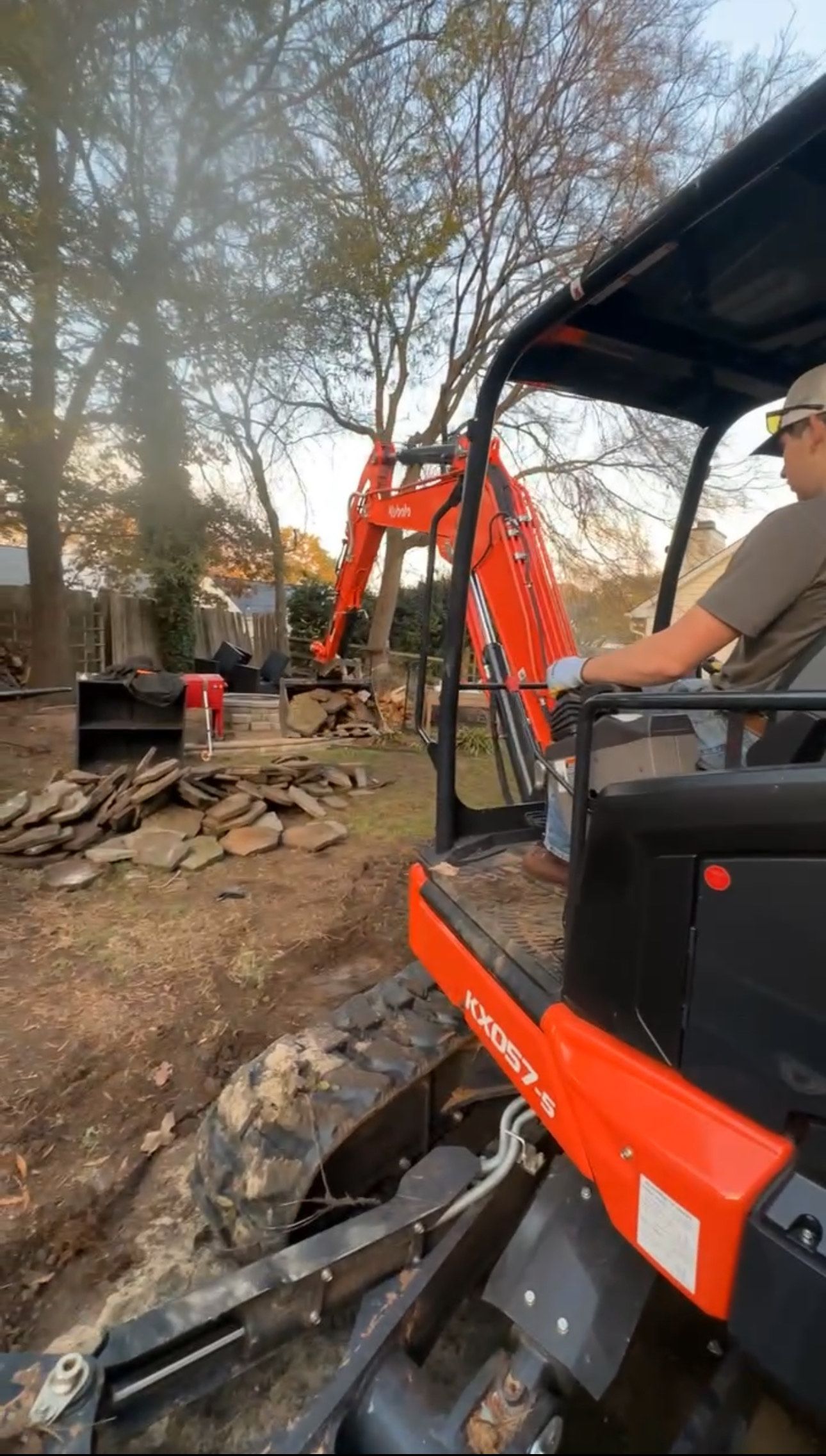 Orange Kubota excavator removing debris with a person at the controls, outdoors.