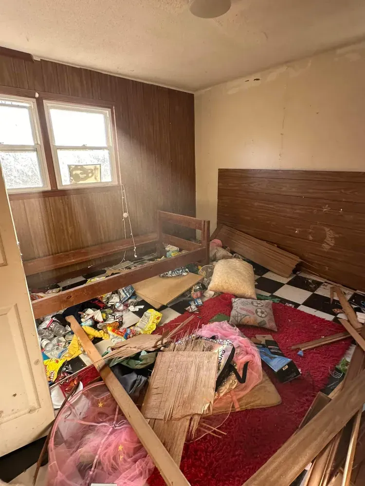 A room with a bed and a lot of trash on the floor.