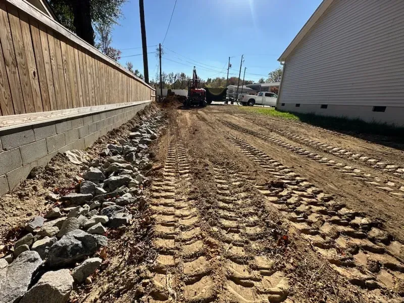 A tractor is driving down a dirt road next to a house.