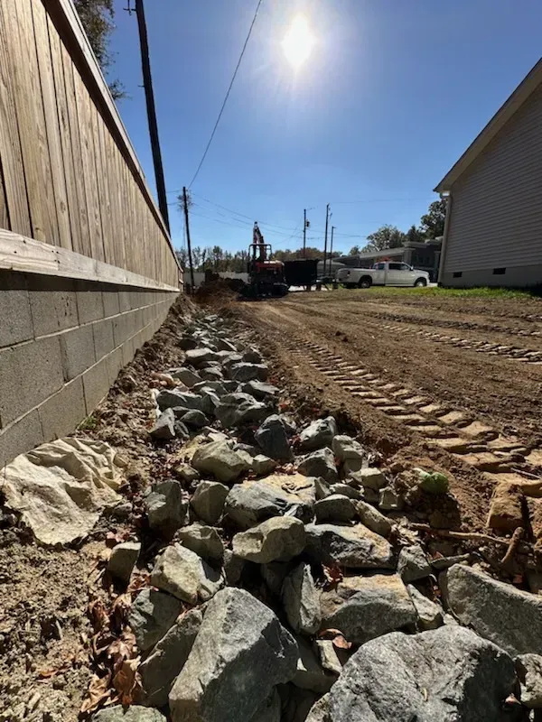 A pile of rocks is sitting on the side of a dirt road next to a house.