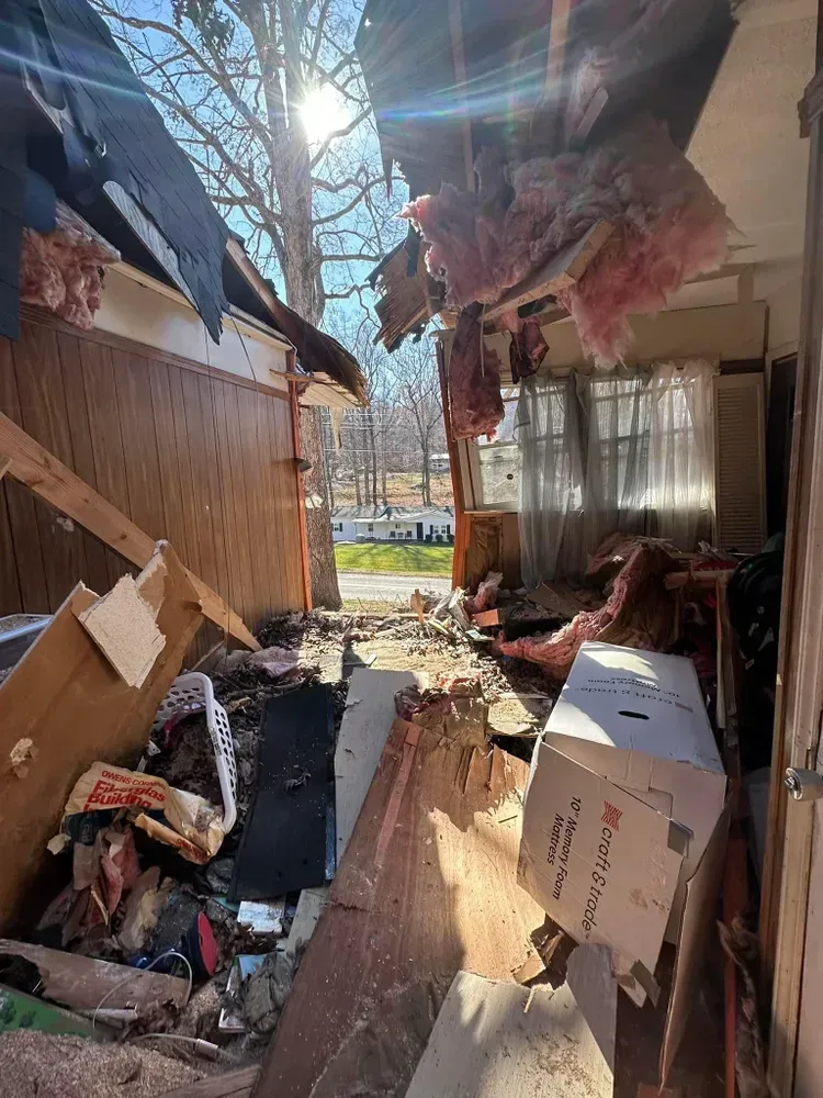 Interior of a damaged building, roof and walls collapsed. Debris and sunlight visible from outside.
