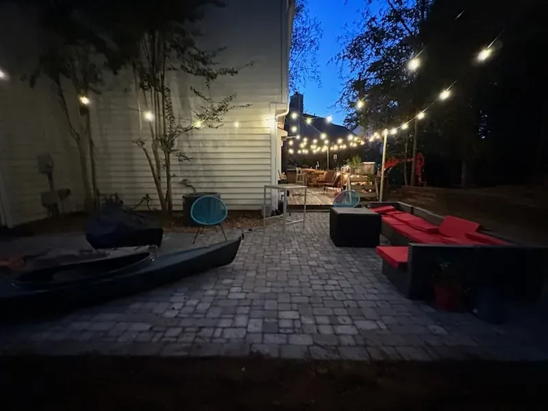 A patio with a kayak , chairs , tables and lights at night.