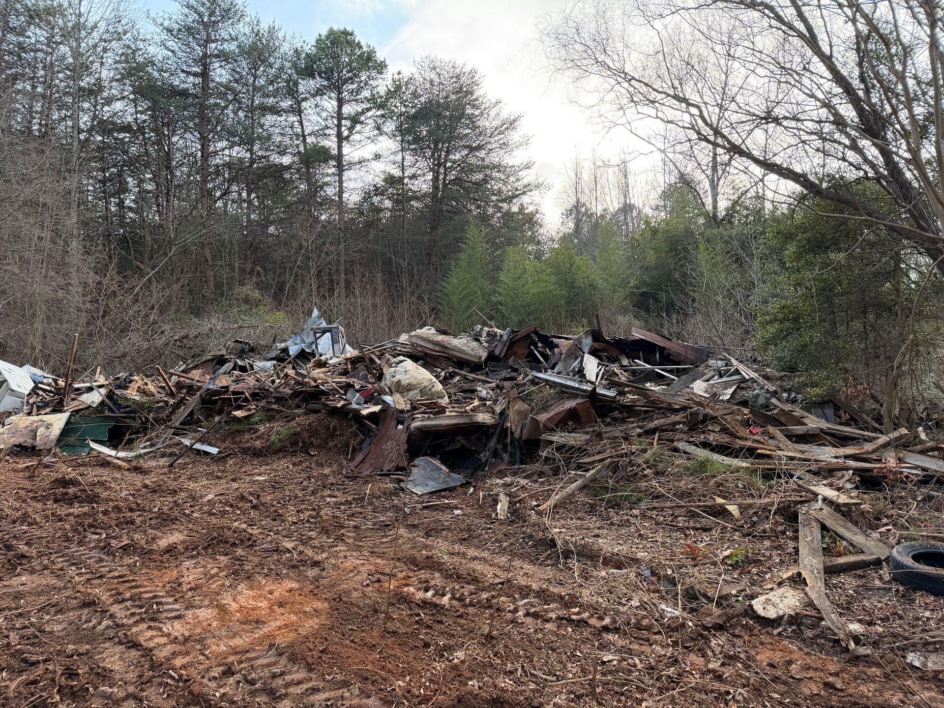 Pile of trash and debris in a wooded area beside a dirt clearing