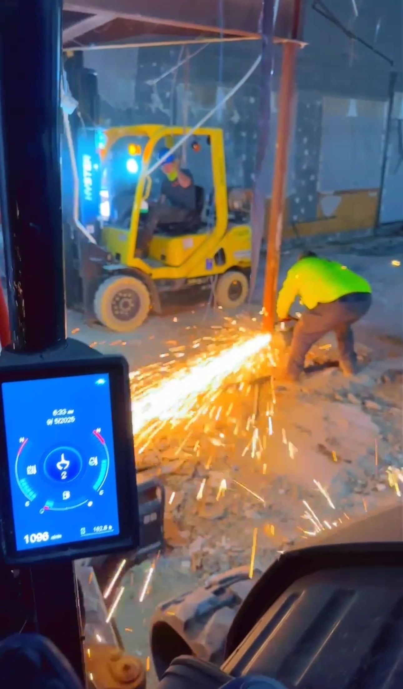 Construction worker cutting metal with sparks flying, forklift in background.