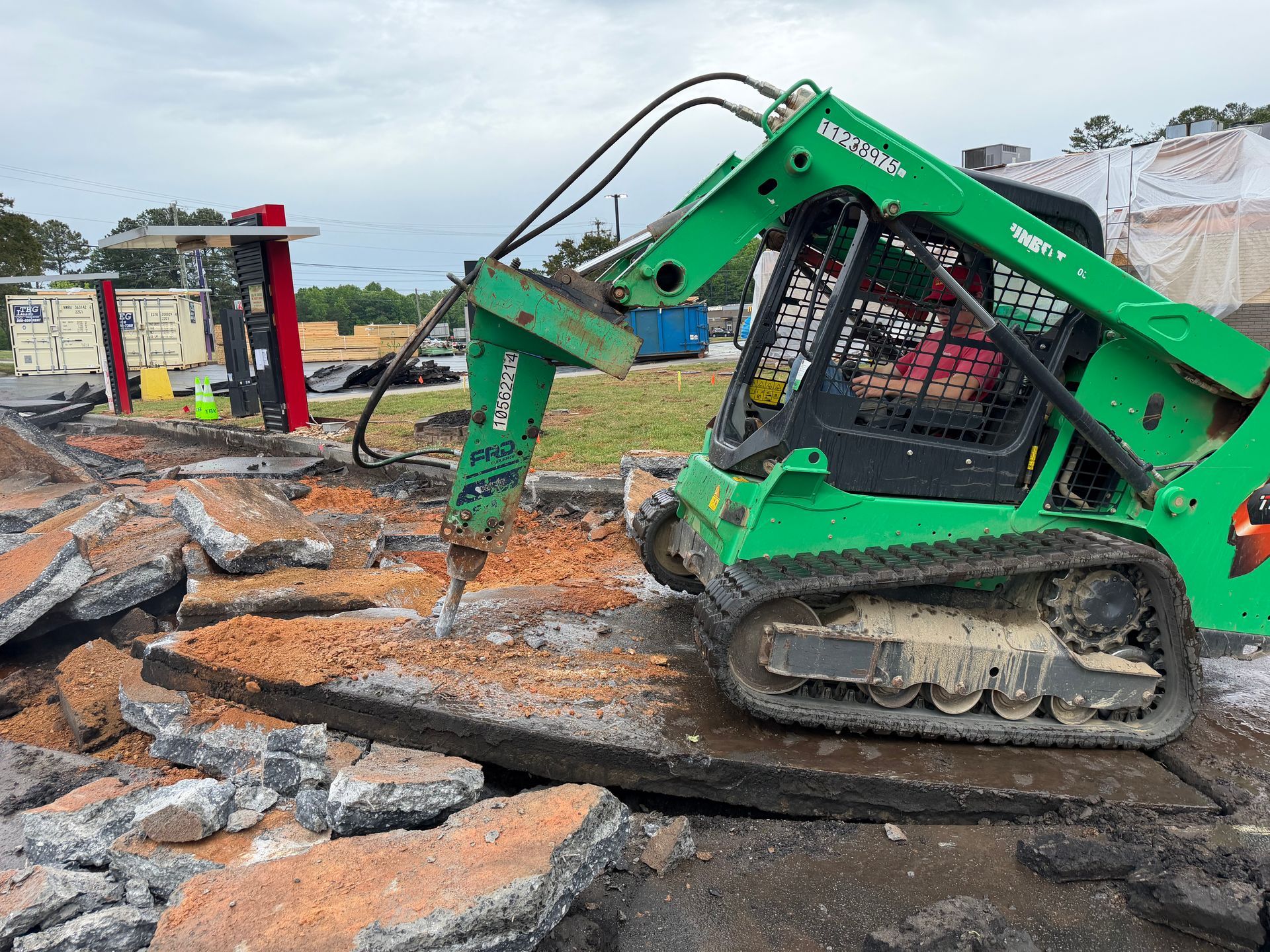 Green skid steer clearing debris over broken asphalt at a construction site