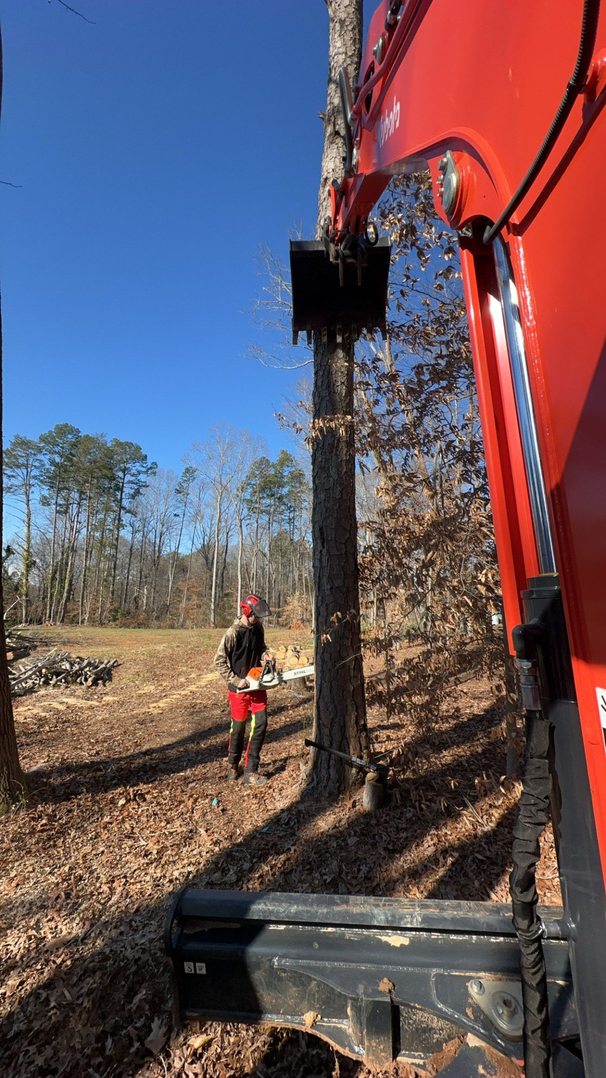 A man is standing next to a red excavator in a field.