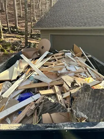 A dumpster filled with a lot of wood is in front of a house.