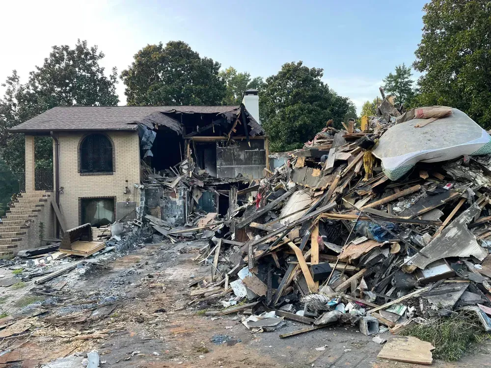 A house heavily damaged by fire, with charred remains and debris piled in front.
