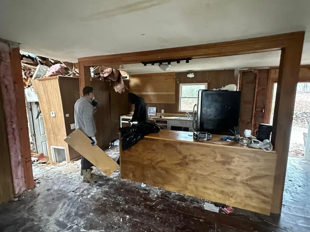 A man is carrying a piece of wood in a kitchen.