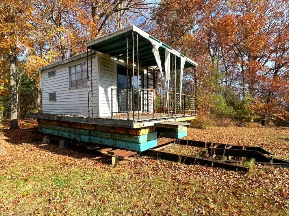 A small house is sitting on top of a trailer in a field.