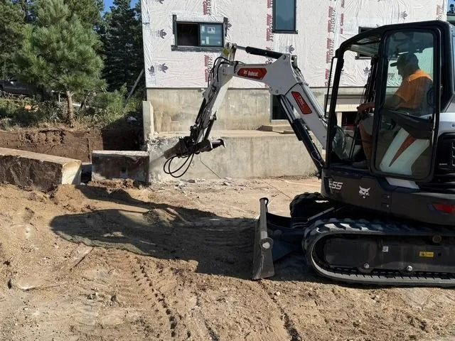 Compact excavator digging dirt beside a house at a construction site
