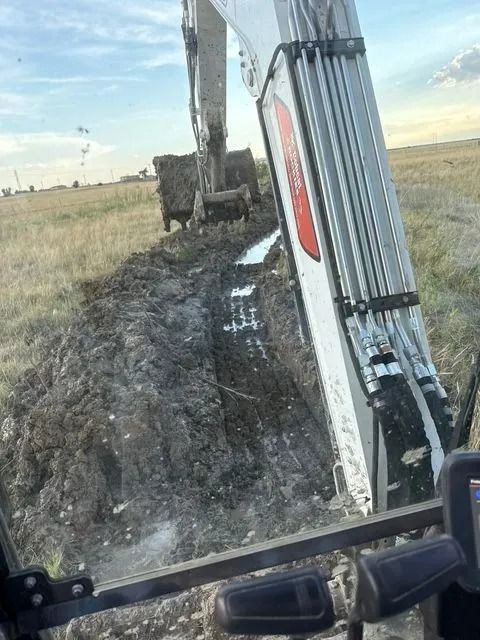 Excavator digging muddy trench beside a field at sunset