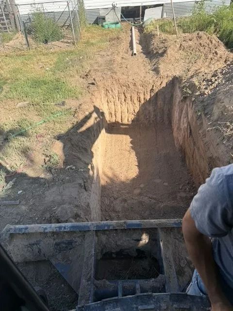 Deep trench excavation on a dirt lot, viewed from the edge with a worker and equipment in the foreground