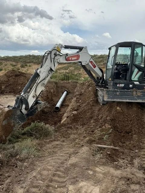 Excavator digging a trench in a muddy field under cloudy skies