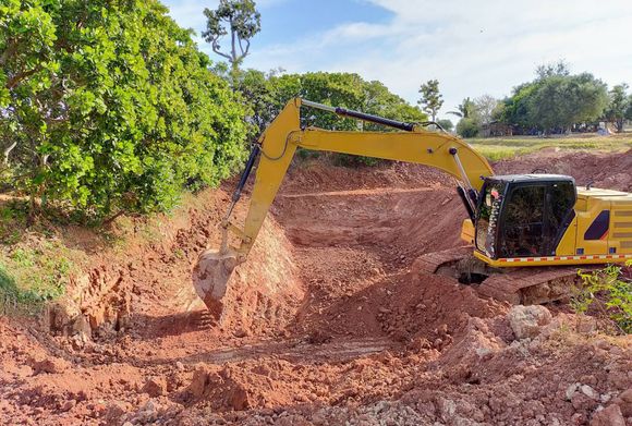 Yellow excavator digging dirt beside a wooded embankment on a construction site