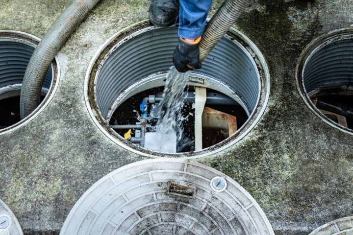 Worker washing a large concrete manhole opening with a hose and spray.