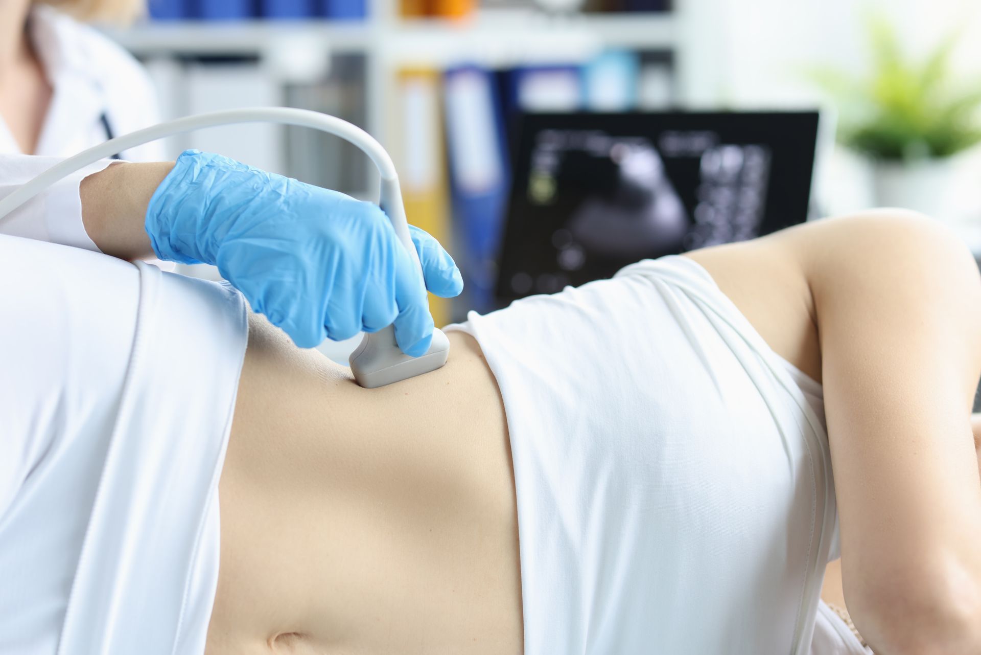 A male doctor in blue scrubs does a kidney ultrasound on an older patient. A male doctor in blue scrubs does a kidney ultrasound on an older patient.
