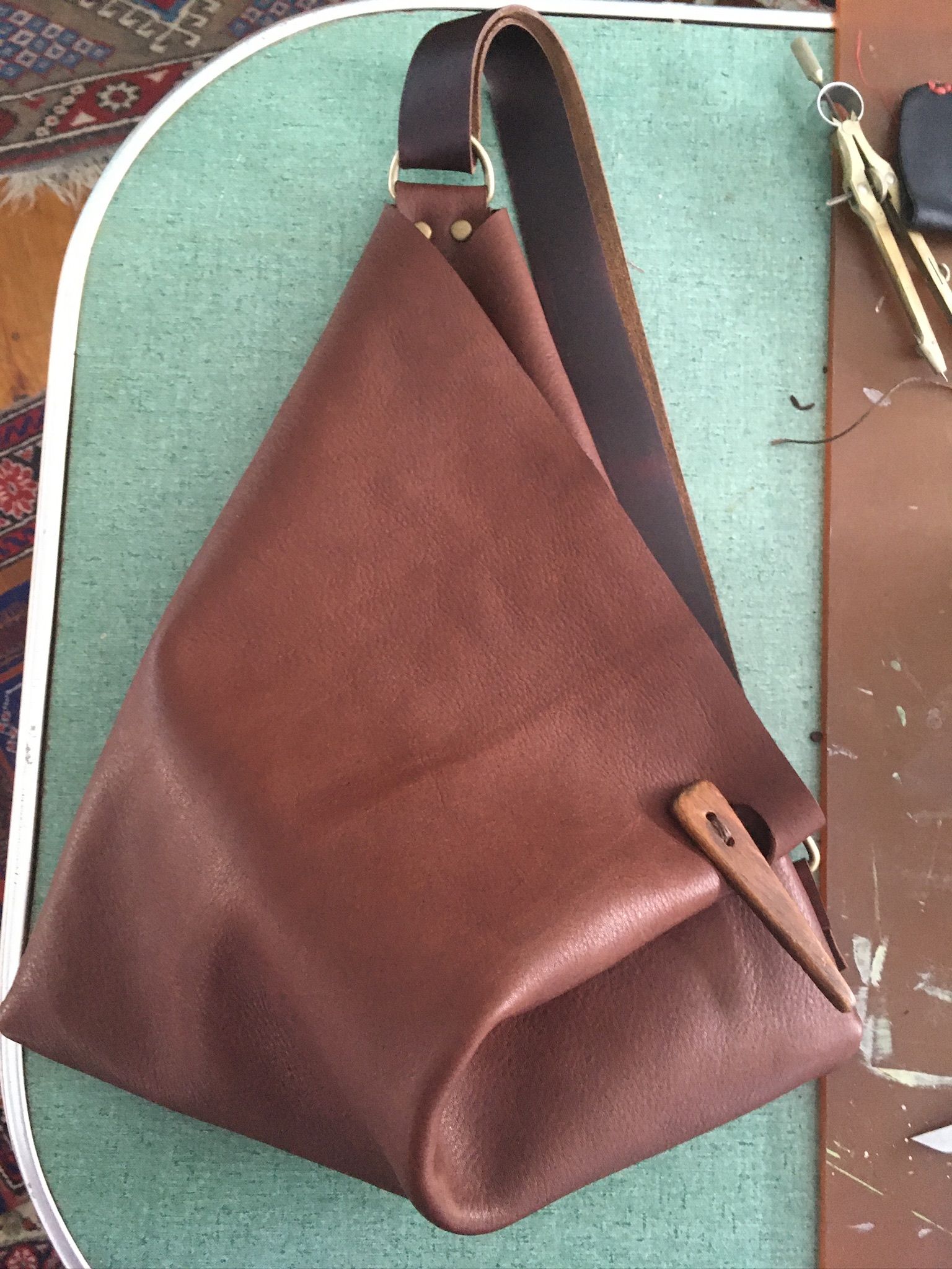 A fold over top, fortune cookie style, leather shoulder bag with wooden button closure