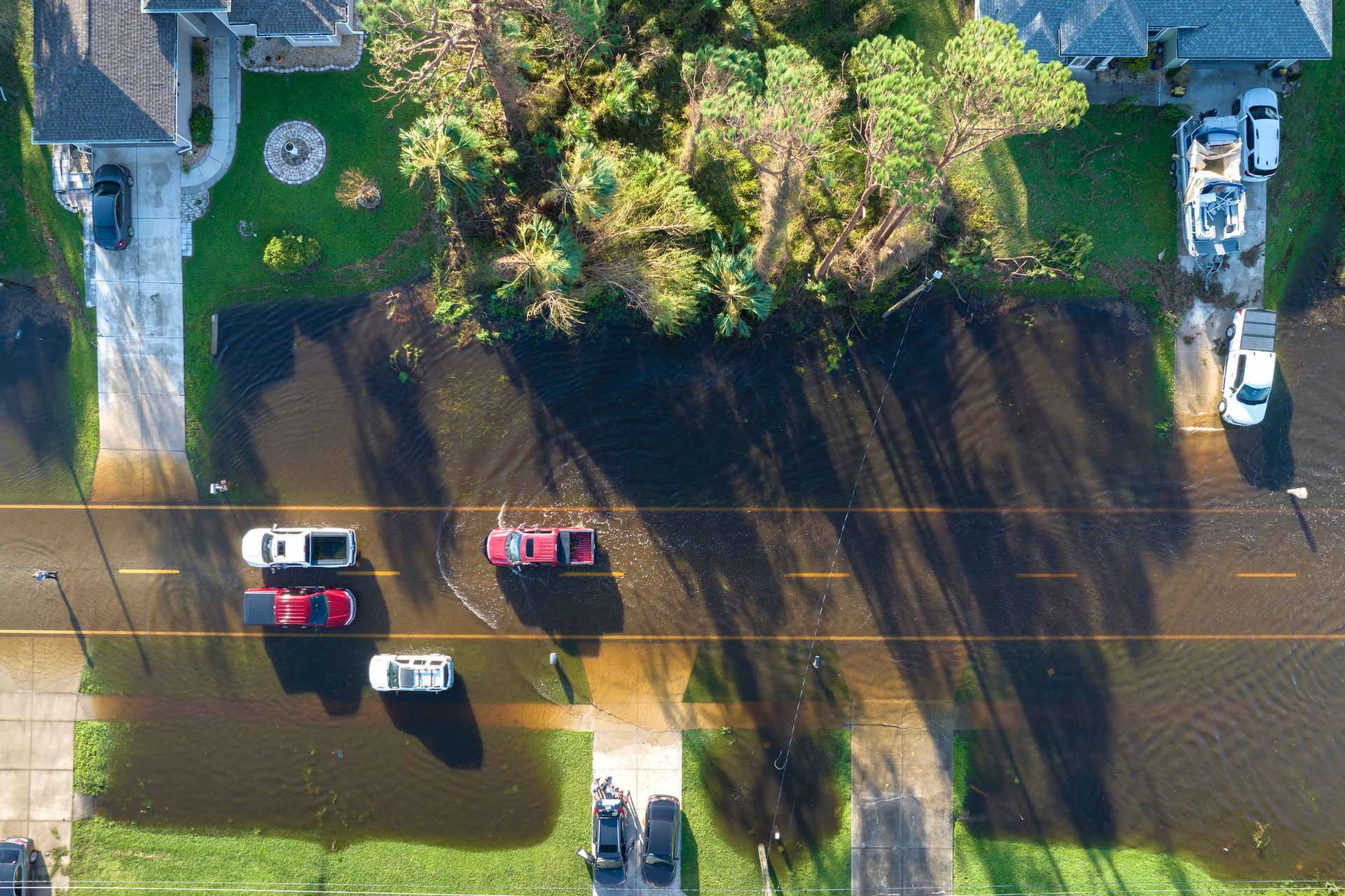 An aerial view of a flooded neighborhood with cars parked on the side of the road.