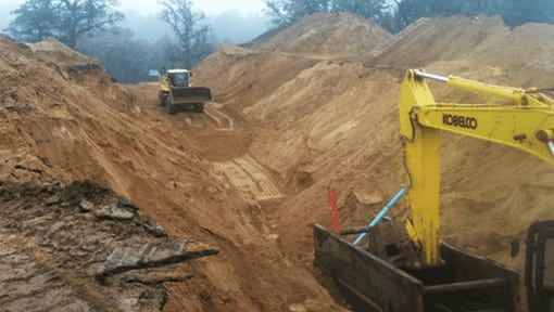 A yellow excavator is digging a trench in a pile of dirt.