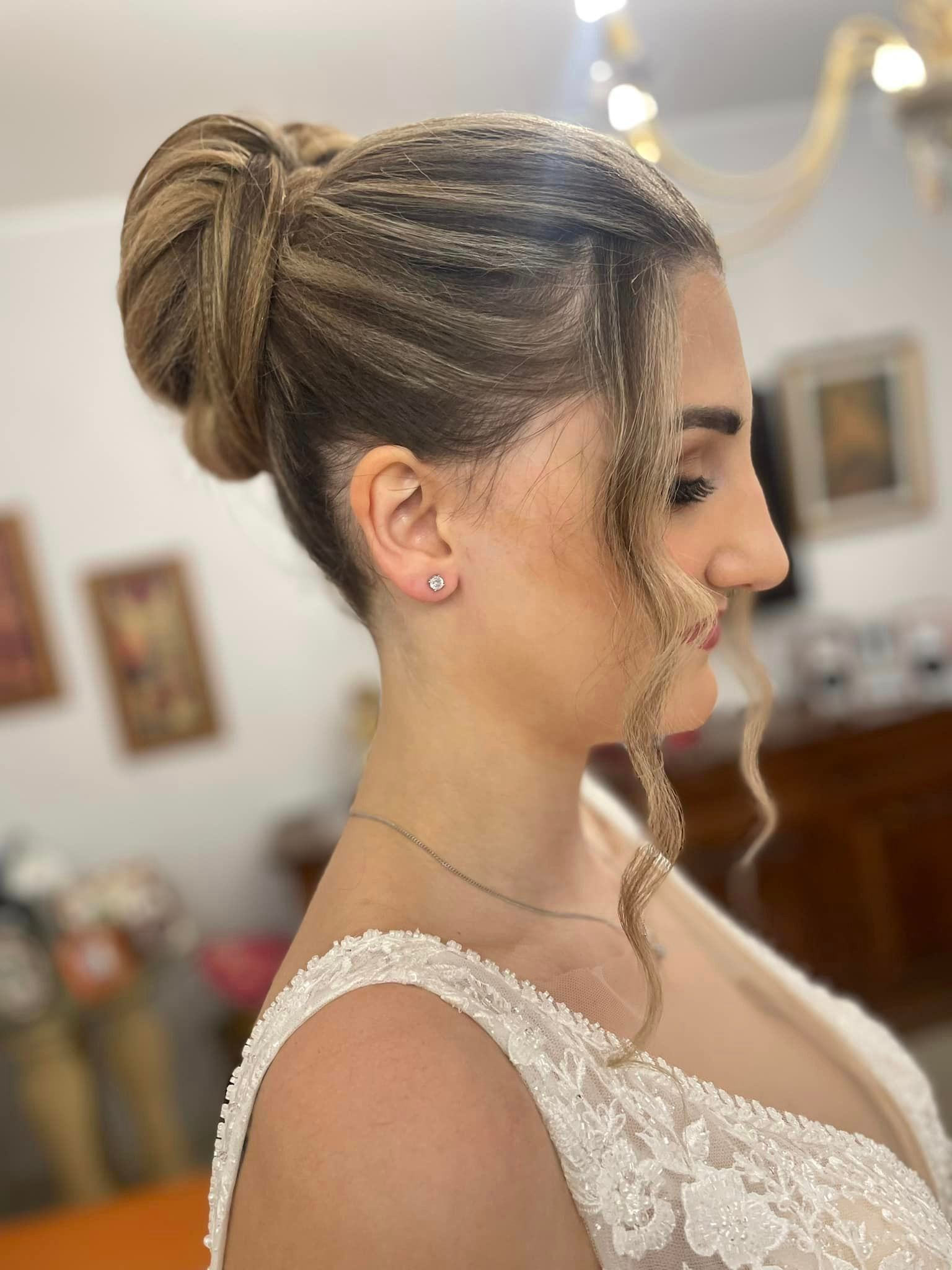 Donna con acconciatura raccolta e intrecciata, indossa un abito bianco decorato, di profilo.